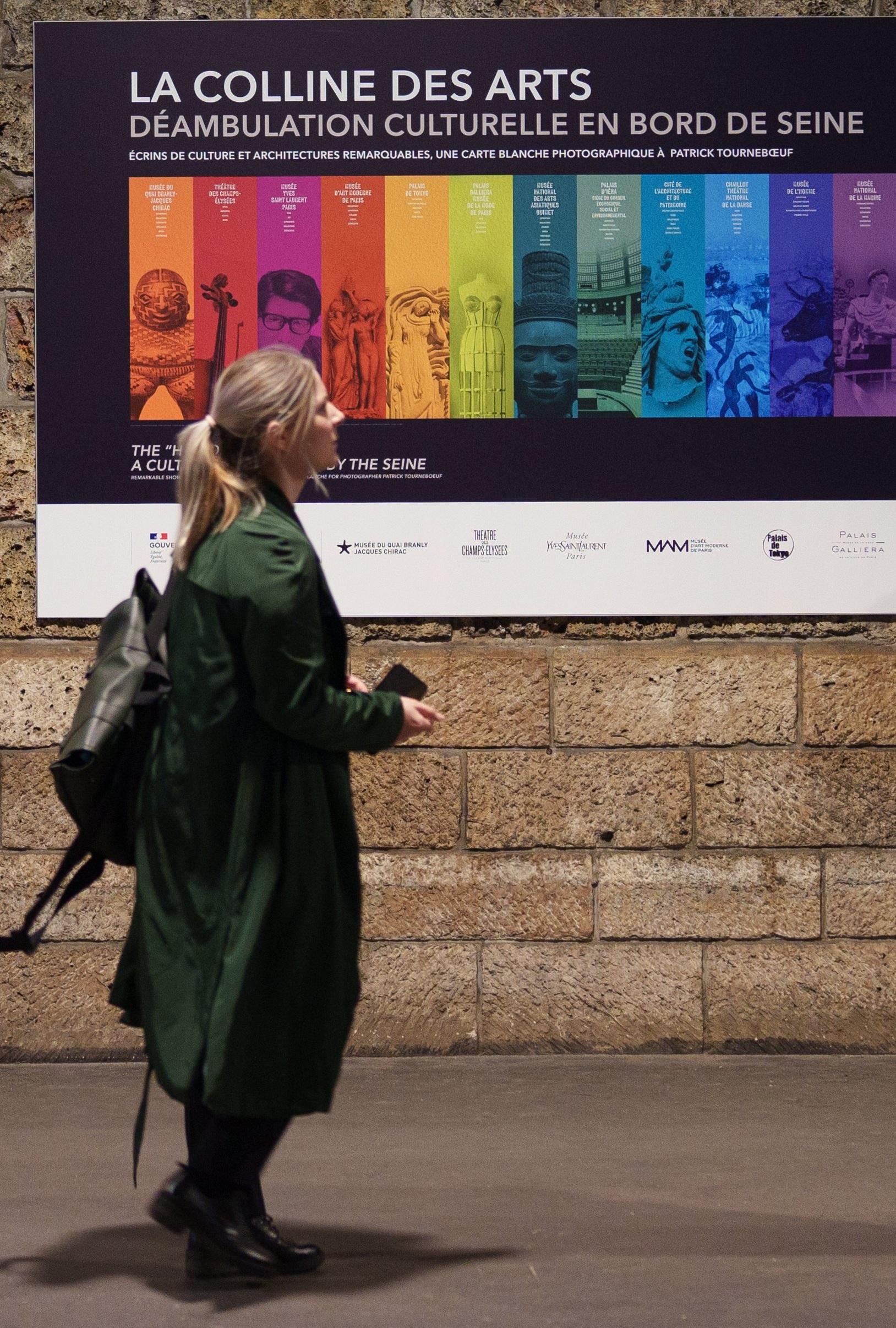 Femme avec une valise a la main devant l'exposition Déambulations Quai de seine