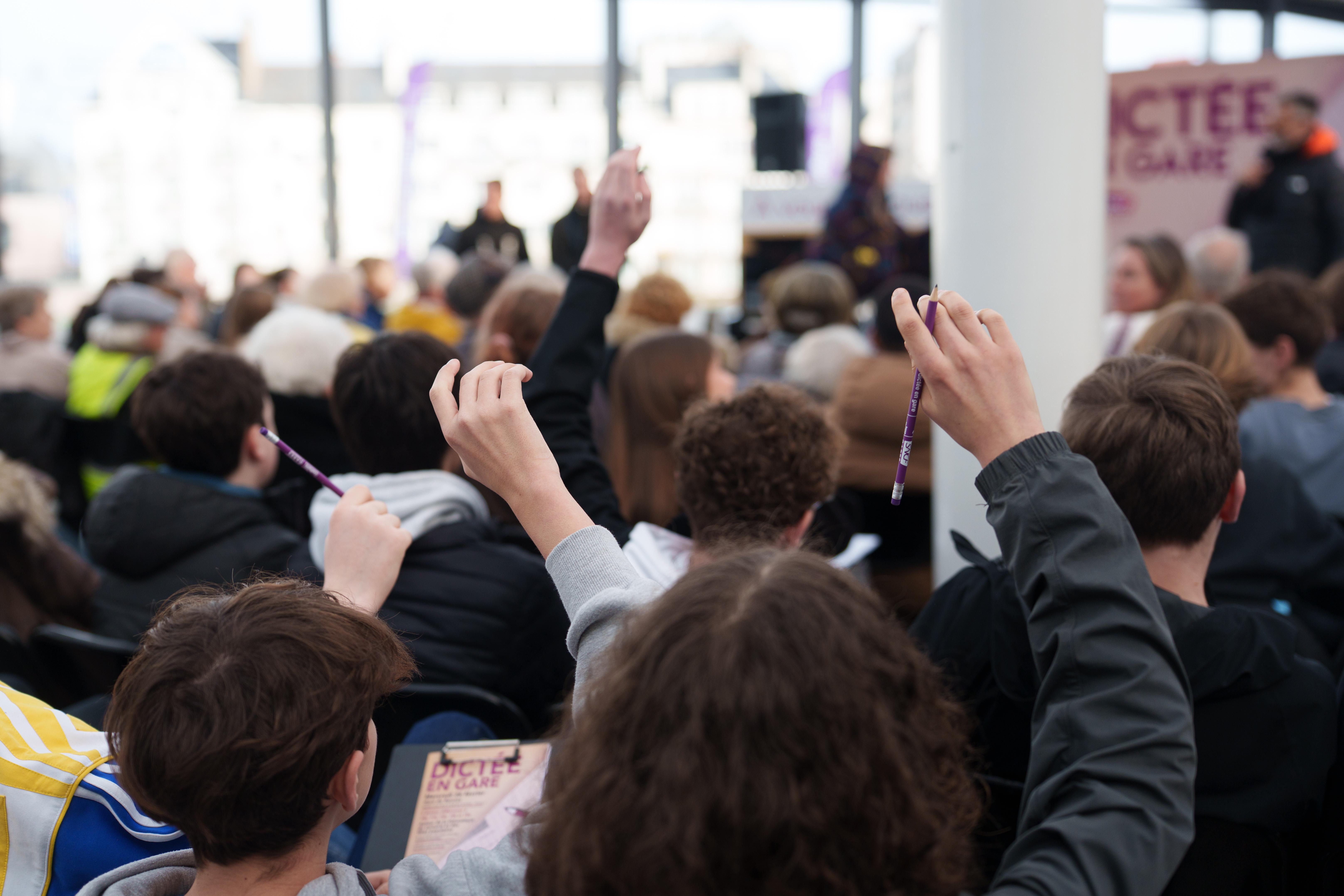 Personnes qui lèvent la main à une dictée en gare de Rennes